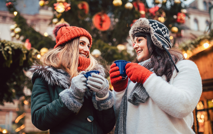 © Kzenon - stock.adobe.com - beste Freunde genießen Glühwein auf dem Weihnachtsmarkt